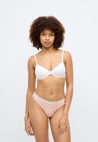 Balts polsterēts krūšturis ar regulējamiem siksniņām, kopā ar rozā apakšbiksēm, kuru jostasvieta ir rotāta ar mežģīnēm. Gluda auduma tekstūra.