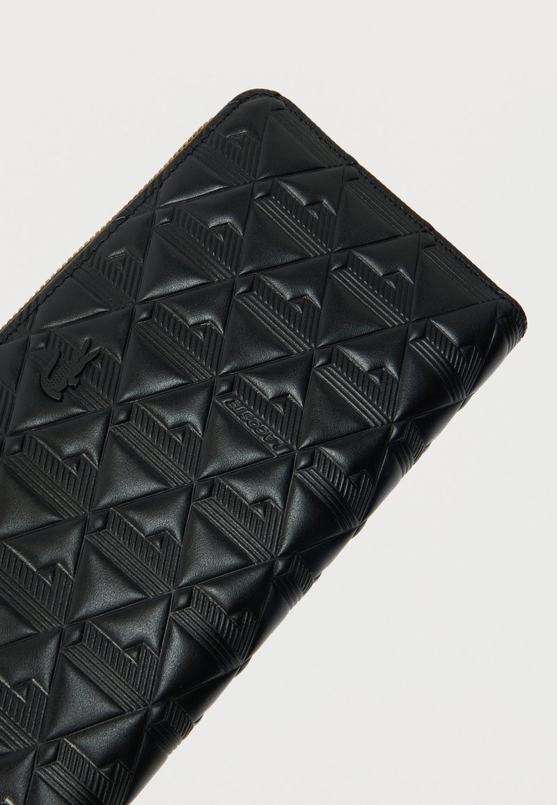 Zwart leren portemonnee met een geometrisch geperst patroon, voorzien van een ritssluiting en logodetails aan de voorkant.