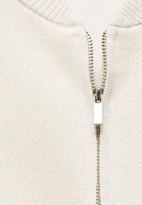Light beige zip-up sweater with a ribbed collar, featuring a silver metal zipper and a smooth, textured knit fabric.