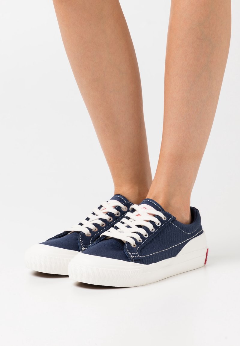 Marina canvas sneakers med vita gummisulor, med vita snören och sömmar. Röd logotypdetalj på hälen.