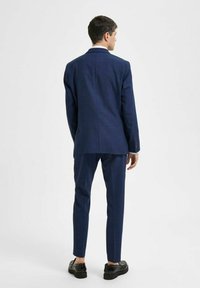 Marinblå skräddarsydd kostym med texturerad finish. Blazern har en enkel slits och slim-fit byxor som smalnar av vid vristerna. Svarta skor fulländar looken.