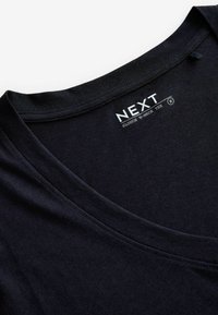 Crna slouch v-neck majica s glatkom teksturom, širokim izrezom i etiketom s "NEXT" logom i detaljima proizvoda.