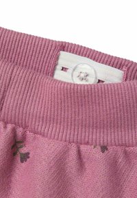 Fascia in tessuto rosa con texture a coste, dotata di chiusura con bottone trasparente e sottile motivo floreale lungo il bordo.