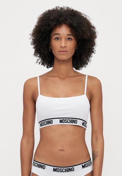 Fehér bralette vékony pántokkal és fekete, Moschino logóval ellátott, márkázott elasztikus szalaggal. Simább textúra, testhezálló dizájn.
