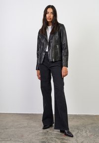 Sort læder bikerjakke med asymmetrisk lynlås, tre lynlåslommer og en cropped pasform; parret med højalmede, vidde sorte jeans.