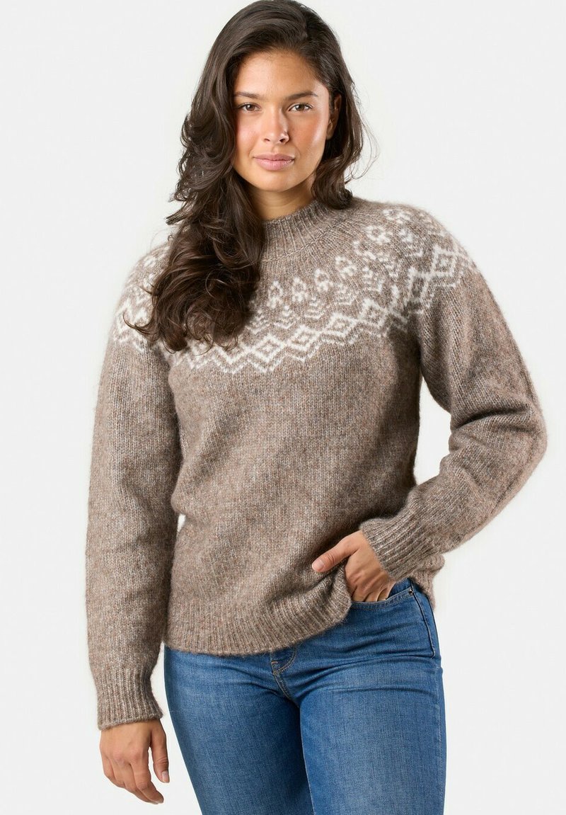 Maglione marrone lavorato a maglia con motivi geometrici bianchi sull'inserto, maniche lunghe, polsini e orlo a costine. Indossato con jeans blu.