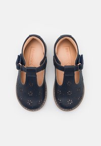 Zapatos de piel azul marino con recortes florales, suela marrón y una correa ajustable. Textura suave con punta redondeada y plantilla acolchada.