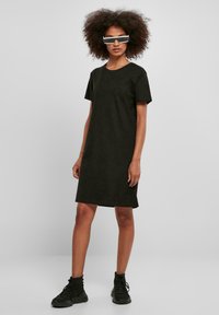 Black short-sleeved dress made of soft fabric, featuring a relaxed fit and a round neck. Paired with sporty black shoes and modern eyewear.