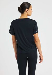 Czarna koszulka sportowa z krótkim rękawem, o luźnym kroju i gładkiej fakturze. Zawiera oznakowanie na lewym rękawie.