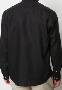 Camisa negra de manga larga hecha de una tela texturada, con un cuello y puños abotonados, con un dobladillo recto y un corte relajado.