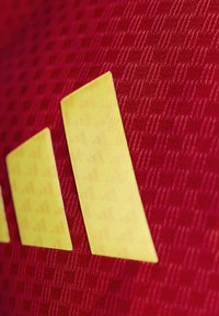 Crvena tkanina s kariranim uzorkom sadrži tri žute pruge u geometrijskom dizajnu, naglašavajući sportski estetski izgled.