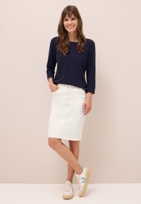 Jupe en denim blanc avec poches avant, assortie à un pull à manches longues bleu marine. Complétée par des baskets beiges avec des accents bleus.