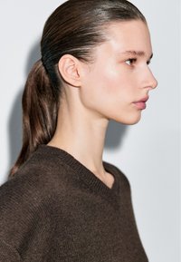 Brauner Strickpullover mit V-Ausschnitt, seitlich an einem Modell präsentiert, das die Textur und das weiche Erscheinungsbild des Stoffes betont.