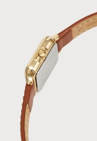 Reloj de metal en tono dorado con caja rectangular, correa de cuero marrón y superficie texturizada. Presenta dos botones de presión en el lateral.