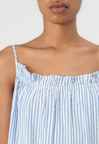 Ľahký, pruhovaný top s modro-bielymi vertikálnymi pruhmi. Má volánový výstrih a tenké ramienka, vyrobený z priedušného materiálu.