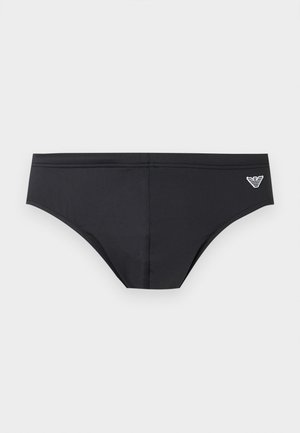 Fekete férfi úszónadrág alacsony derékvágással és kis fehér logóval a jobb oldalon, egyszínű háttér előtt.