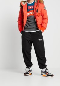 Red puffer jacket with fur-lined hood, gray sweatshirt, black joggers with "DIESEL" logo, and multicolored sneakers with white laces.