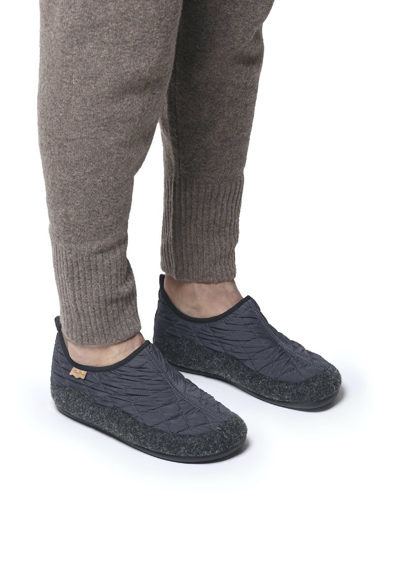Crne pamučne slip-on cipele s teksturiranim sivim filcem na potplatu i stražnjem dijelu. Nosi se s laganim smeškim rebrastim hlačama, ističući dizajn cipela.