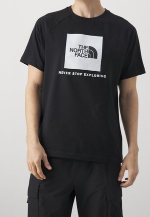 Osoba nosząca czarną koszulkę z białym kwadratowym logo z napisem "The North Face" i tekstem "Never Stop Exploring" z przodu.