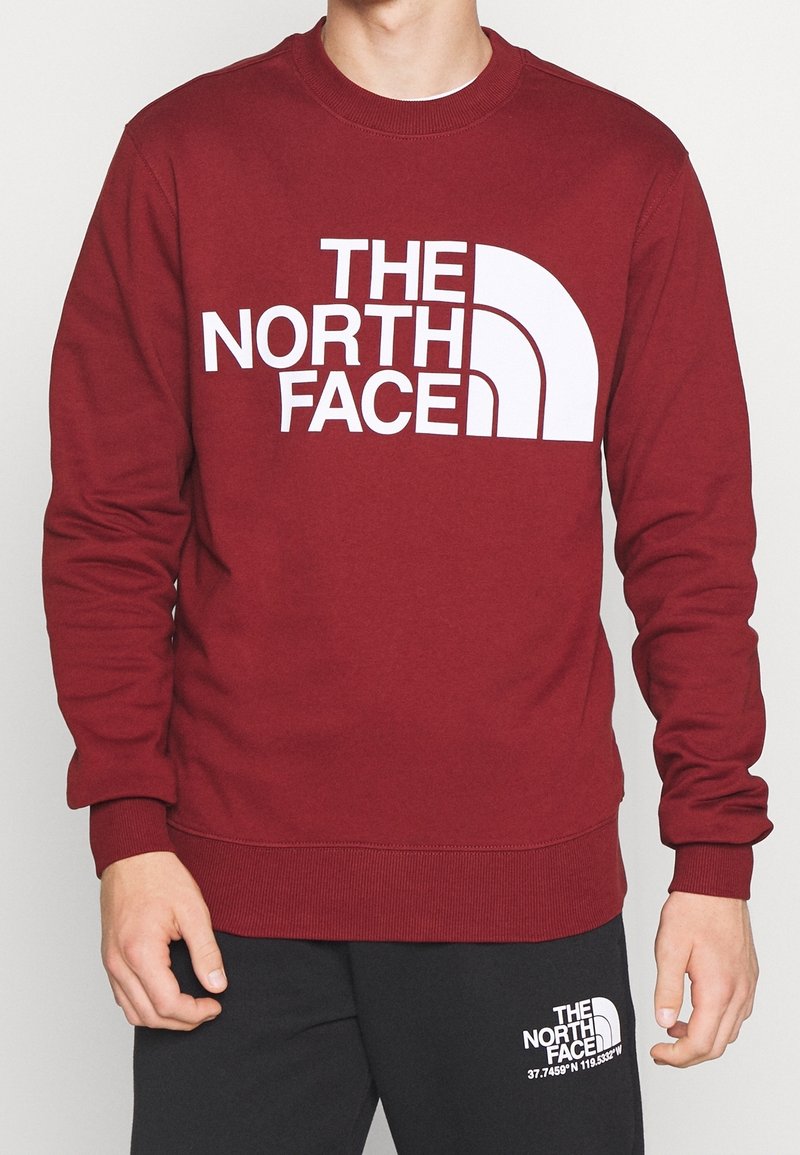 Felpa rossa con grande logo bianco "THE NORTH FACE" e pantaloni neri con un logo più piccolo abbinato e coordinate sulla coscia.
