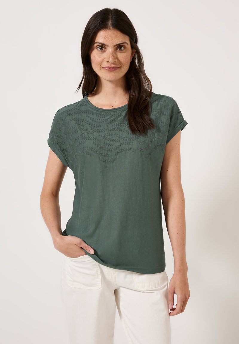 Haut vert à manches courtes avec un motif de vagues texturé sur le devant, fabriqué en tissu doux. Il possède un col rond et une coupe décontractée.