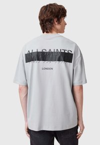 Camiseta gris de gran tamaño con una banda horizontal negra con texto blanco en la parte posterior. Manga corta y un corte relajado. Material de algodón.