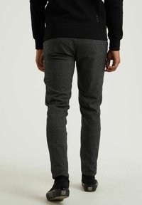Osoba v šedých kostkovaných slim-fit kalhotách, černé mikině a černých slip-on botách, stojící na neutrálním světlém pozadí.