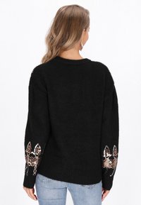 Maglione nero con maniche lunghe e morbide, caratterizzato da design in paillettes sui polsini. Tessuto testurizzato con scollatura rotonda.