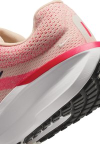 Gros plan d’un talon de chaussure de course tricotée rose et beige avec une semelle intermédiaire blanche et une semelle extérieure noire texturée.