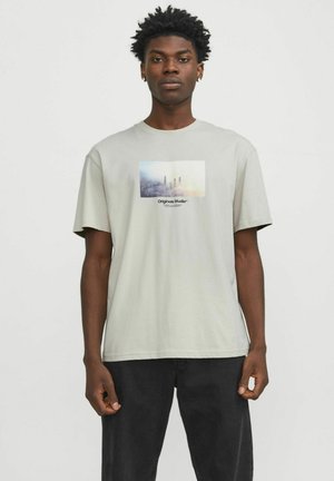 Camiseta de algodón gris claro con un estampado gráfico rectangular que presenta un paisaje urbano y el texto "Originals Studio" en el centro. Mangas cortas.