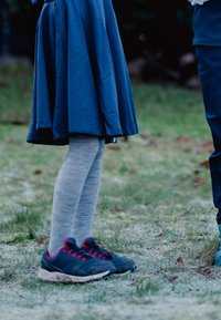Sneakers i mørkegrå med røde detaljer, parret med lysegrå strukturerede strømpebukser, sammen med et marineblåt knælangt nederdel i et græsset miljø.