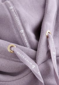 Svetlo fialová mikina s textúrovanou tkaninou, ktorá má zlaté očká a krémové šnúrky s logom s nápisom "by Ted Baker".