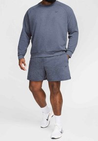 Nike graues Sweatshirt- und Shorts-Set mit strukturiertem Stoff, rundem Ausschnitt und seitlichen Taschen, kombiniert mit weißen Sportschuhen.