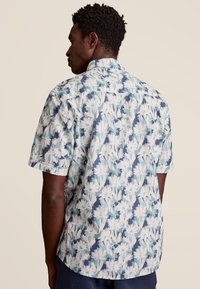 Korte mouw shirt van lichtgewicht stof met een bloemenpatroon in wit, blauw en groen op een donkere marineblauwe achtergrond.