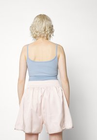 Světle modrý top na ramínka s tenkými popruhy, spárovaný s volnými, růžovými saténovými šortkami s elastickým pasem a bočními kapsami.