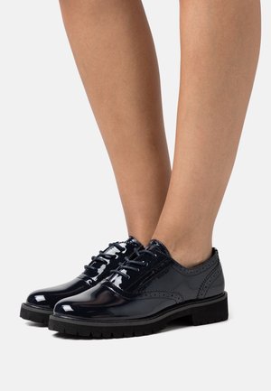 Brogues in vernice nera con accenti texturizzati e punta rotonda, dotati di lacci neri e una spessa suola in gomma con battistrada.