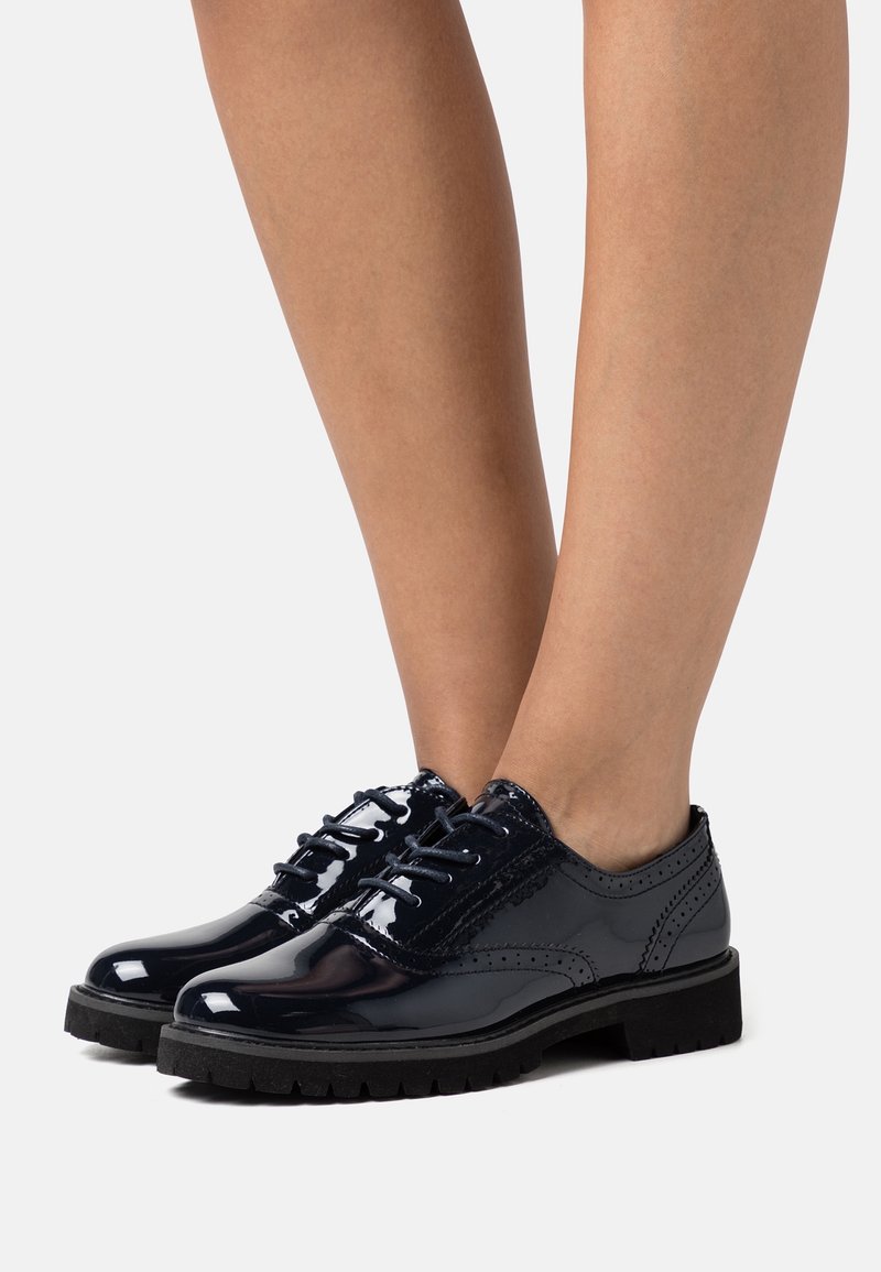 Brogues in vernice nera con accenti texturizzati e punta rotonda, dotati di lacci neri e una spessa suola in gomma con battistrada.