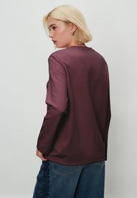 Hosszú ujjú felső mély bordó anyagból, kerek nyakkivágással és laza szabással. Világos koptatott farmerrel párosítva, laza megjelenéshez.