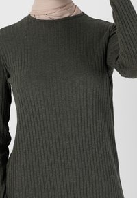 Haut vert foncé à manches longues côtelé avec un col rond, fabriqué à partir d'un tissu doux. Présente des lignes verticales texturées et une silhouette ajustée.