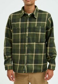 Grün-beige karierter Flanellhemd mit zwei Fronttaschen, schwarzen Knöpfen und einem Kragen. Weicher Stoff, knöpfbarer Front.