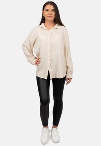 Camicia button-up color crema con un tessuto strutturato e piccoli punti bianchi, abbinata a leggings neri e sneaker bianche.
