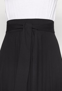 Mustat korkeavyötäröiset hameet, joissa on leveä vyötärönauha solmittu solmuun, yhdistetty valkoiseen sisäänpuettuun toppiin.