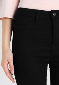 Svarta denimjeans med en åtsittande design. Har fem fickor, bältesloopar och en frontknäppning. Slät textur, ingen synlig slitage.