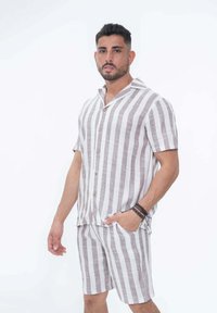 Chemise en lin à manches courtes et short assorti en beige clair avec des rayures verticales marron foncé. Dispose d'un col décontracté et de fermetures à boutons.