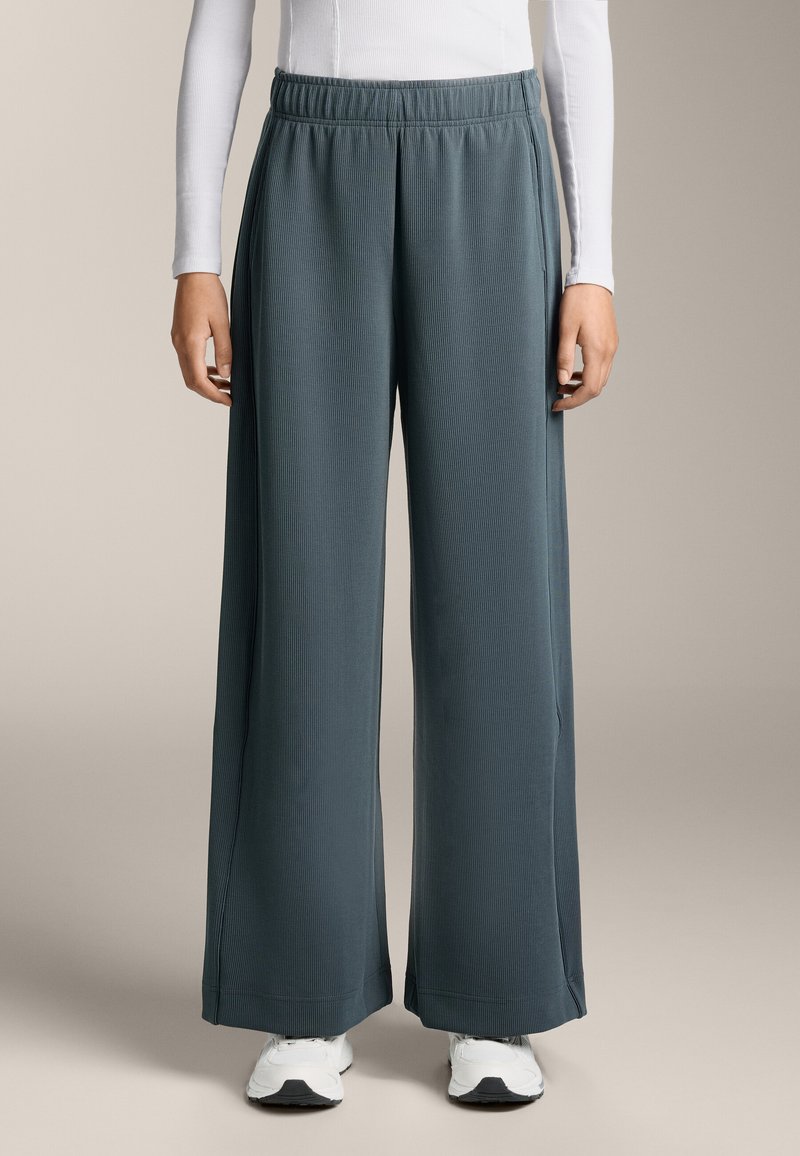 Široké nohavice z texturovanej tmavomodrej látky s elastickým pásom, doplnené o biele topánky, na svetlom pozadí.