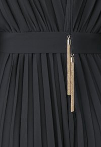 Abito plissettato nero con una texture di tessuto liscia, caratterizzato da una ampia cintura in vita e dettagli con nappe dorate che pendono dalla cintura.