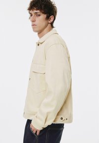 Beige, oversized jakke med en trykknapkrave, to for-lommer og løs pasform. Fremstillet af glat stof med et minimalistisk design.