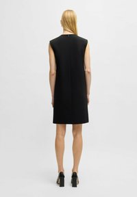 Schwarzes ärmelloses Kleid mit geradem Schnitt, knielangem Saum und einem diskreten Reißverschluss auf der Rückseite. Glattes Material mit matter Oberfläche.