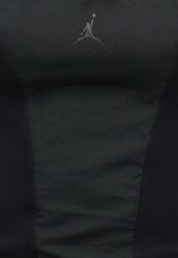 Μαύρο ύφασμα με λεπτό ανάγλυφο σχέδιο και μικρό γκρι λογότυπο Jumpman ενός παίκτη μπάσκετ που είναι στη μέση ενός άλματος κρατώντας μια μπάλα.