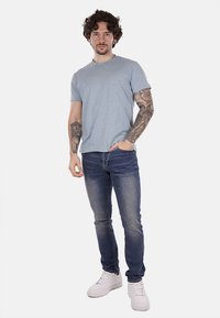 T-shirt azzurro chiaro a maniche corte abbinato a jeans blu scuro e sneakers bianche; presenta un collo rotondo e una silhouette aderente.